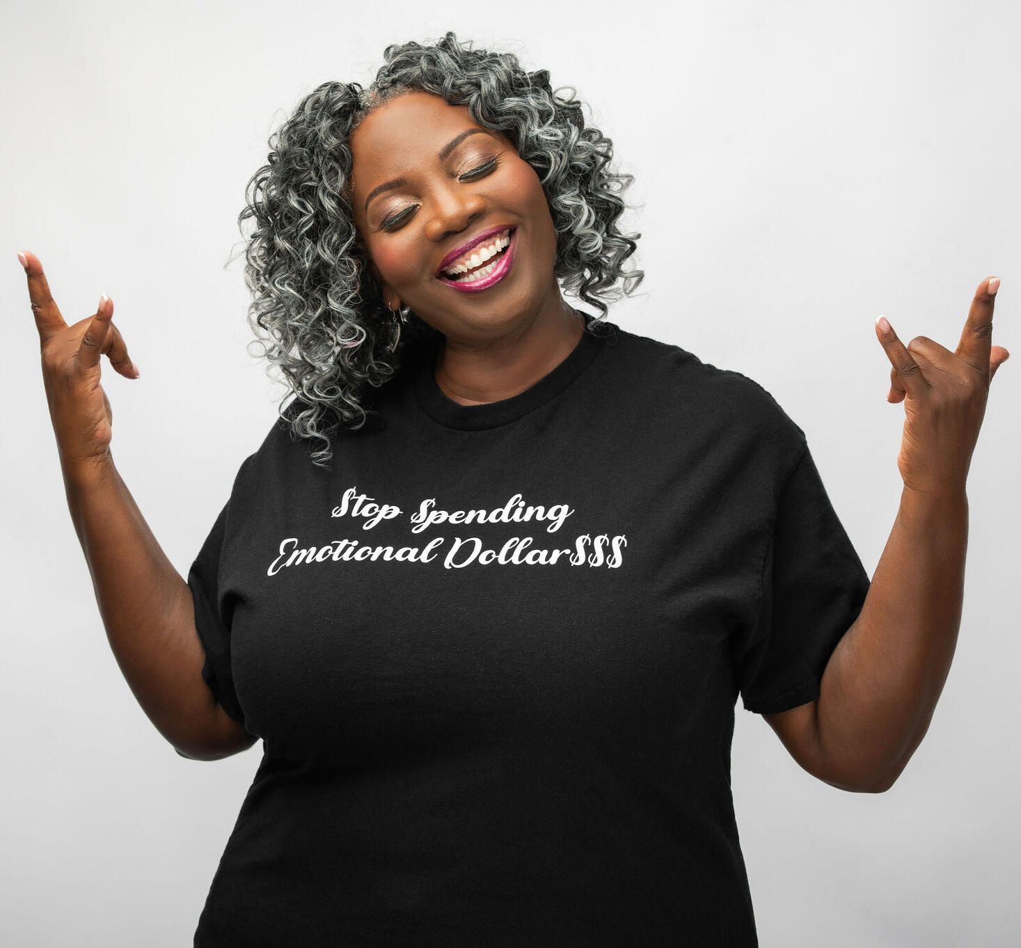 Regina Nunnally Regina wearing a black t-shirt with the words "Stop Spending Emotional Dollars $$$" printed in white, Regina is holding her hands up in the air with lets rock hand gestures.
