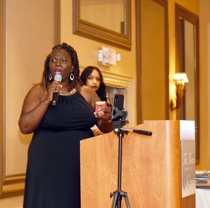 Regina Nunnally wearing a Blue t-shirt with the words "You should be Here" printed on the front and wearing sunglasses.